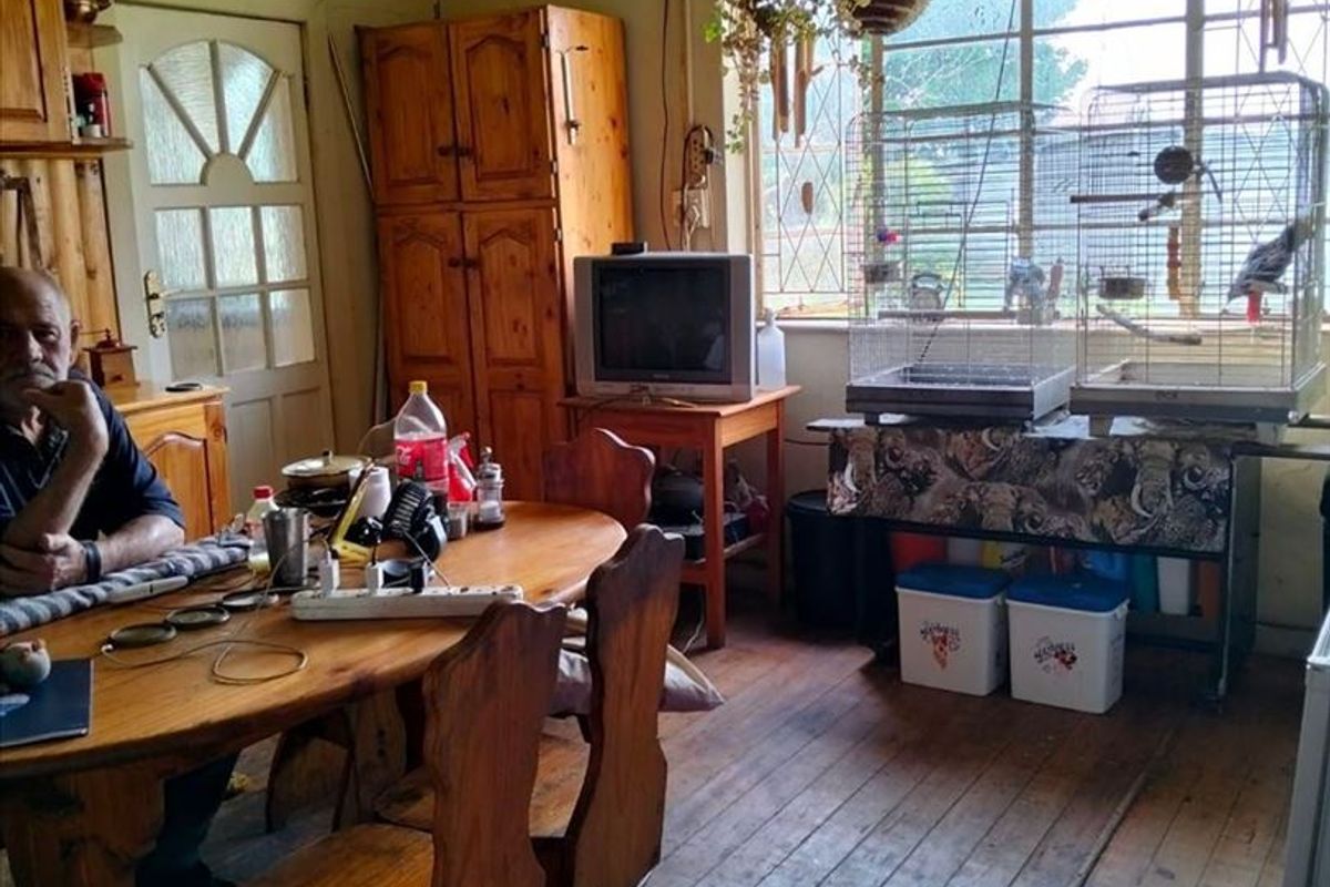 A rustic dining area featuring original timber flooring, steel-framed windows, and built-in wooden cabinetry, offering a traditional farm-style aesthetic in need of refurbishment.