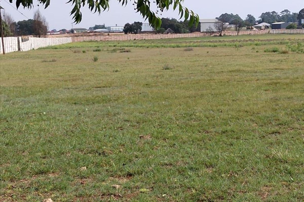 A wide, open grassy field on the farm property, enclosed by perimeter fencing with distant structures visible in the background.