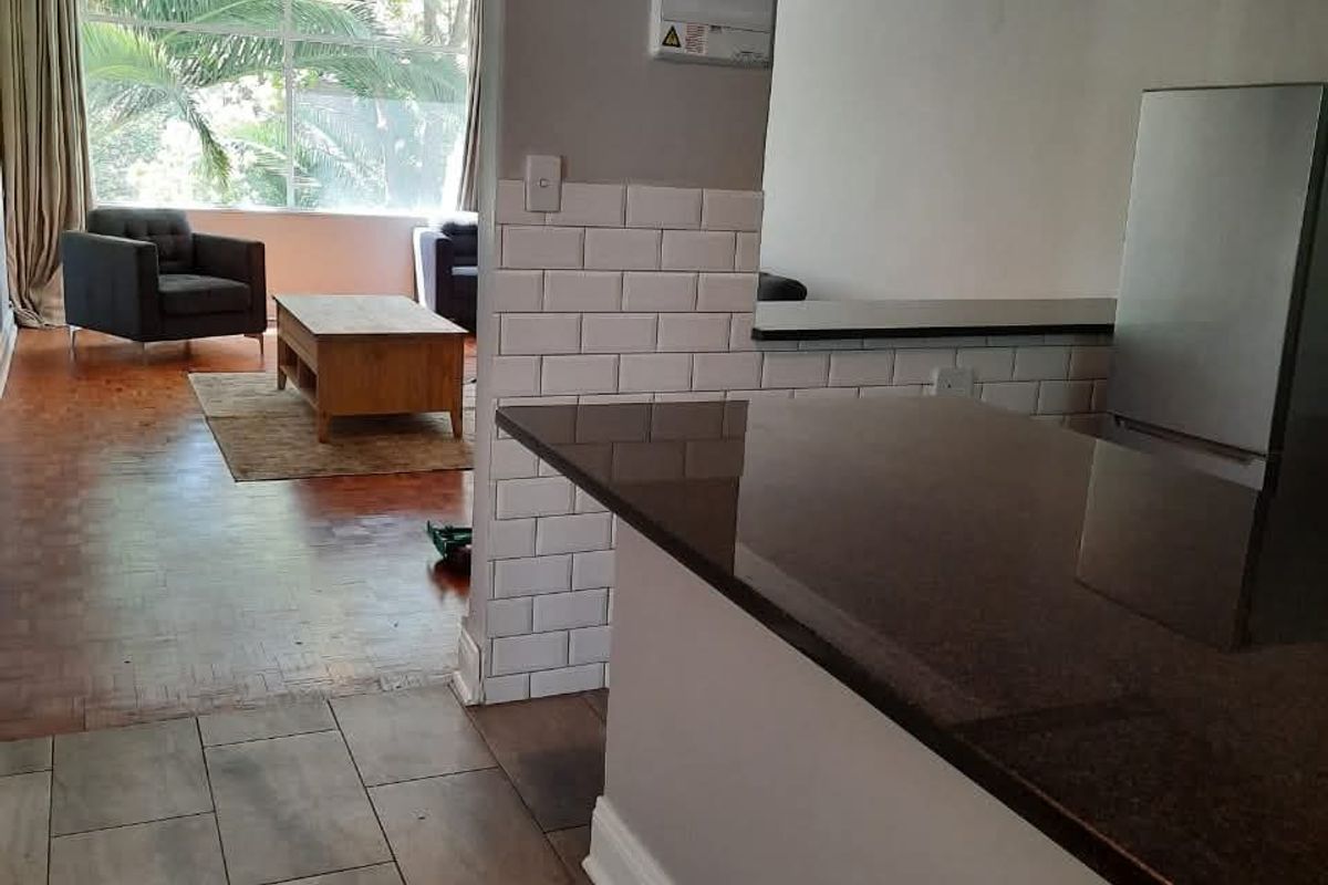 Open plan kitchen and living area featuring a breakfast bar with granite countertops, subway tile backsplash, and parquet flooring in the lounge.