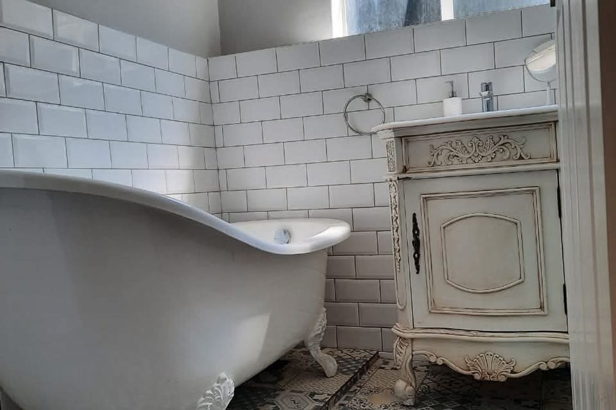 A charming bathroom featuring a classic clawfoot bathtub, patterned floor tiles, and white subway wall tiling with a vanity unit.