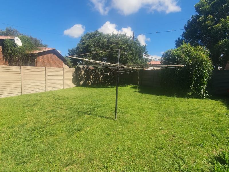 A spacious backyard featuring a well-maintained lawn, enclosed by precast concrete boundary walls and equipped with a central rotary clothesline.