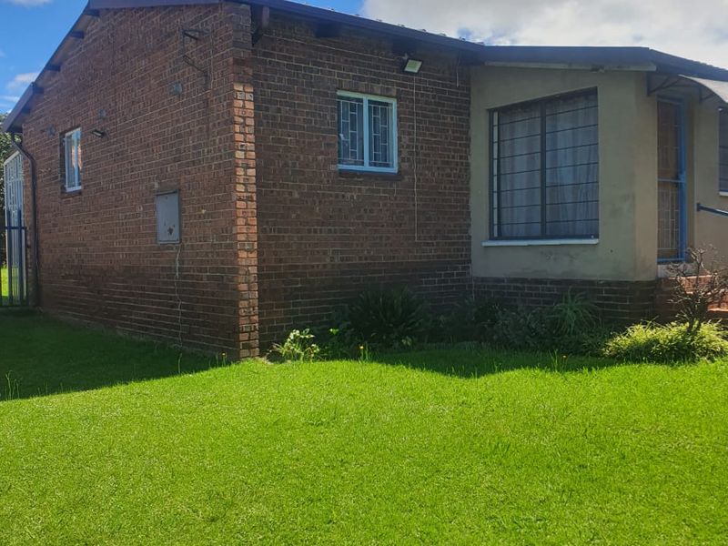 A view of the front exterior of a face brick house featuring security bars on windows and a well-maintained lawn.