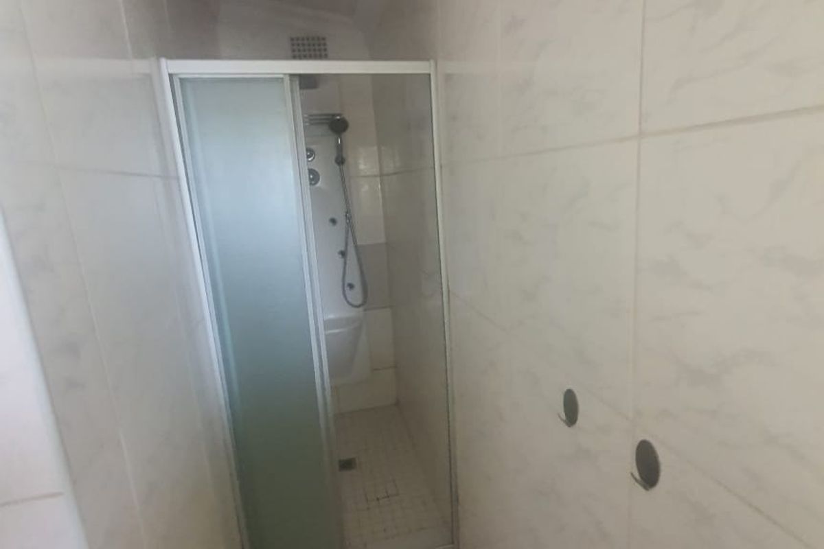 A small bathroom featuring a shower enclosure with tiled walls and flooring, currently requiring minor repairs to wall fixtures.