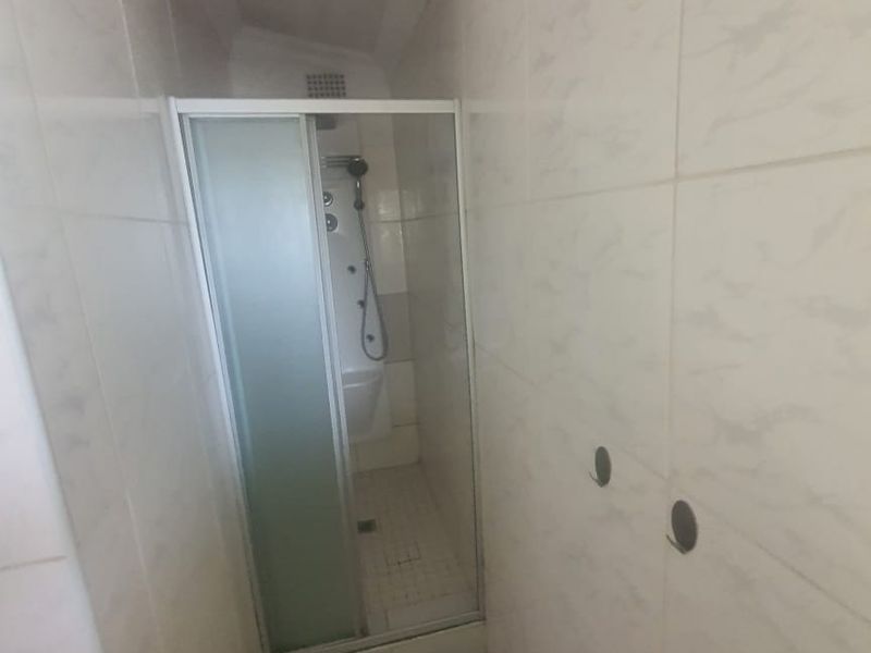 A small bathroom featuring a shower enclosure with tiled walls and flooring, currently requiring minor repairs to wall fixtures.