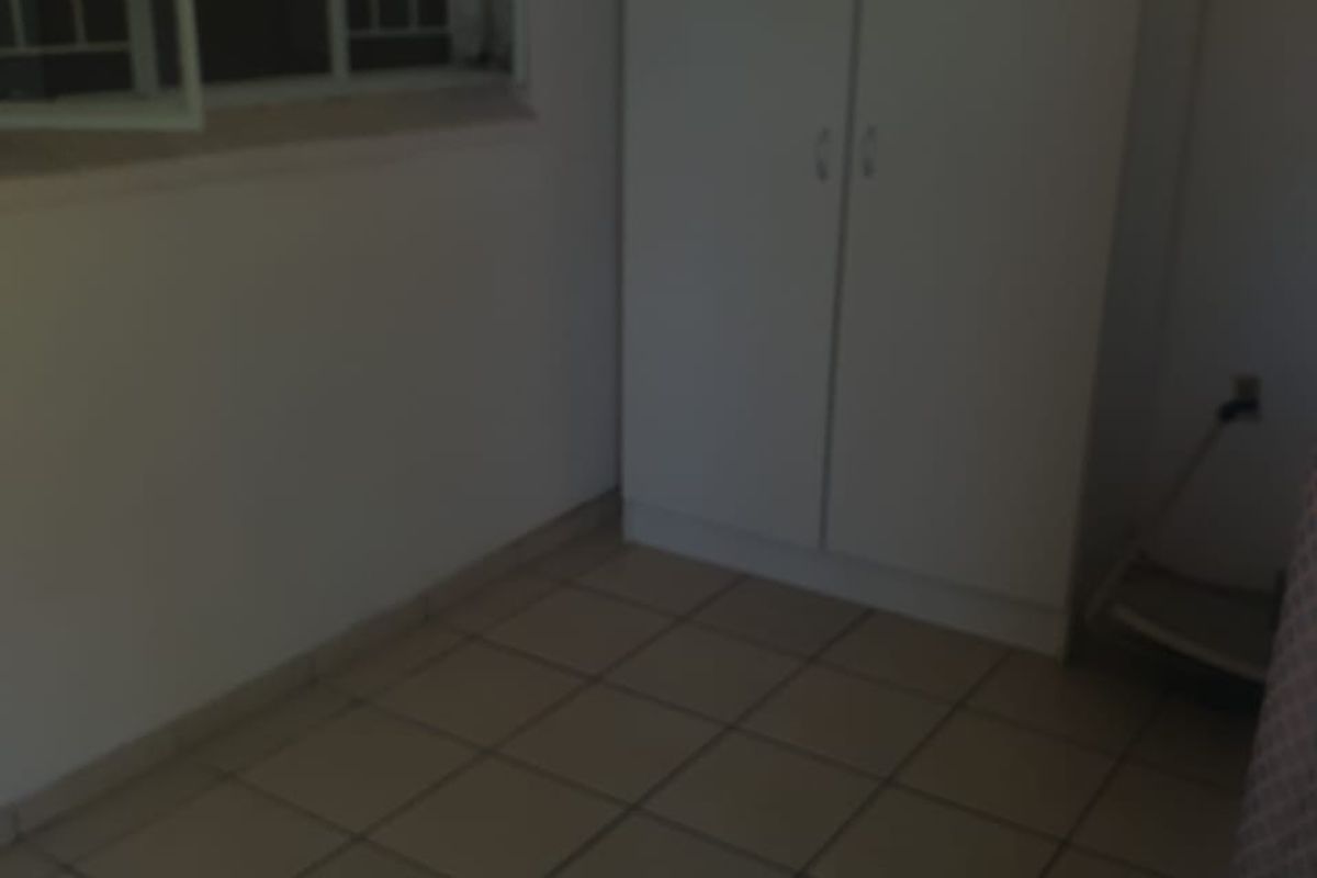 A simple, empty bedroom featuring tiled flooring, a built-in wardrobe, and a window fitted with security bars.