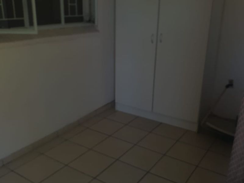 A simple, empty bedroom featuring tiled flooring, a built-in wardrobe, and a window fitted with security bars.