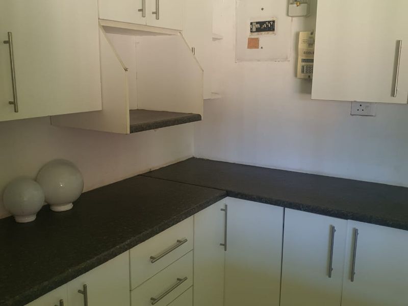 A functional scullery area featuring white built-in cabinetry, dark laminate countertops, and tiled flooring, providing additional storage and workspace.