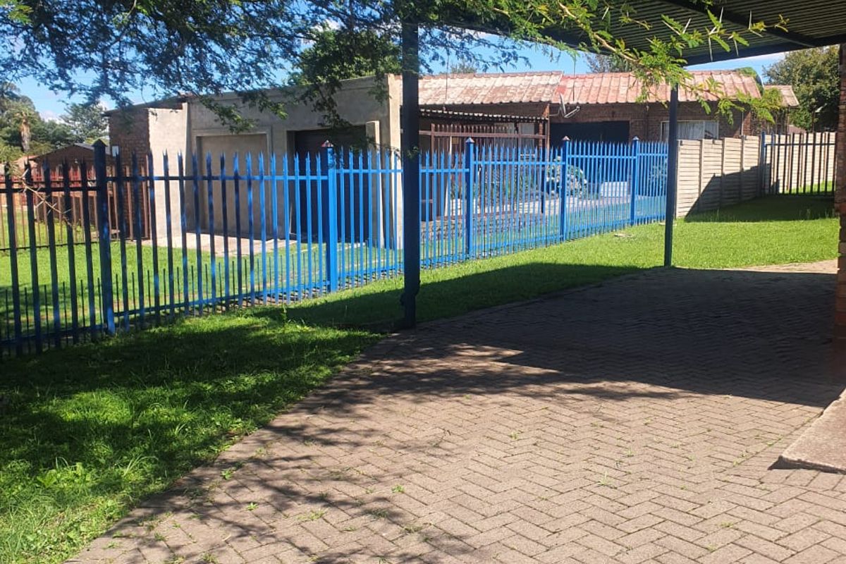 Rear exterior view featuring a paved driveway, carport, and secure steel palisade fencing surrounding the property grounds.