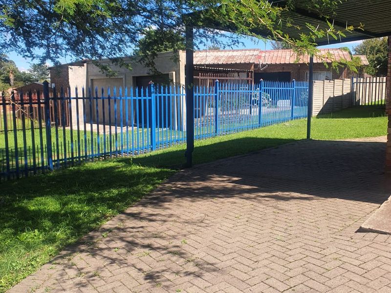Rear exterior view featuring a paved driveway, carport, and secure steel palisade fencing surrounding the property grounds.