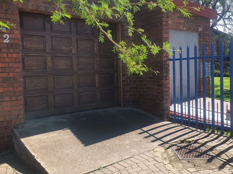 Exterior view of a brick garage featuring a sectional door, concrete ramp, and paved driveway with adjacent steel security fencing.