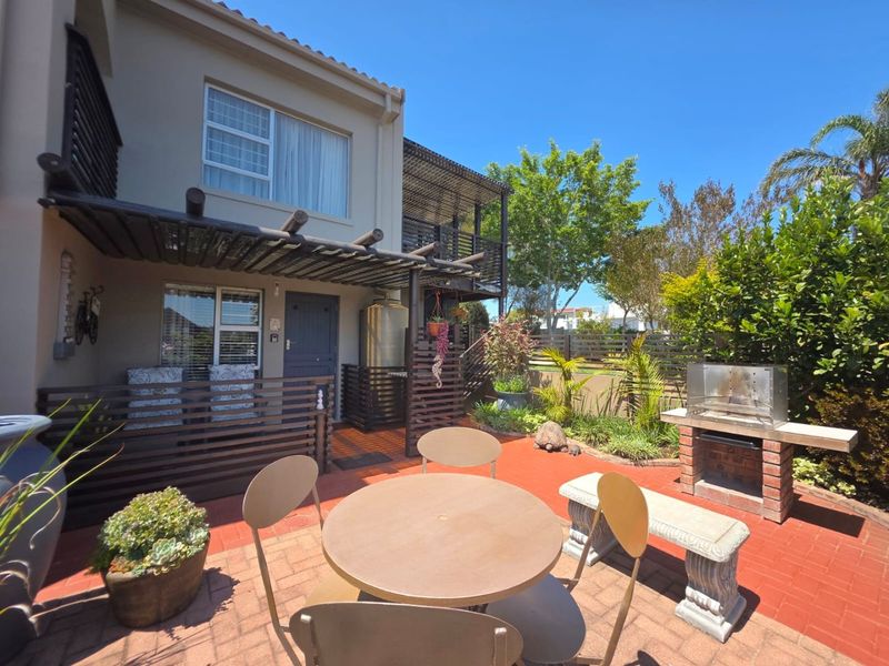 A well-maintained outdoor patio area featuring a timber pergola, built-in brick braai, and paved flooring, ideal for outdoor entertaining.
