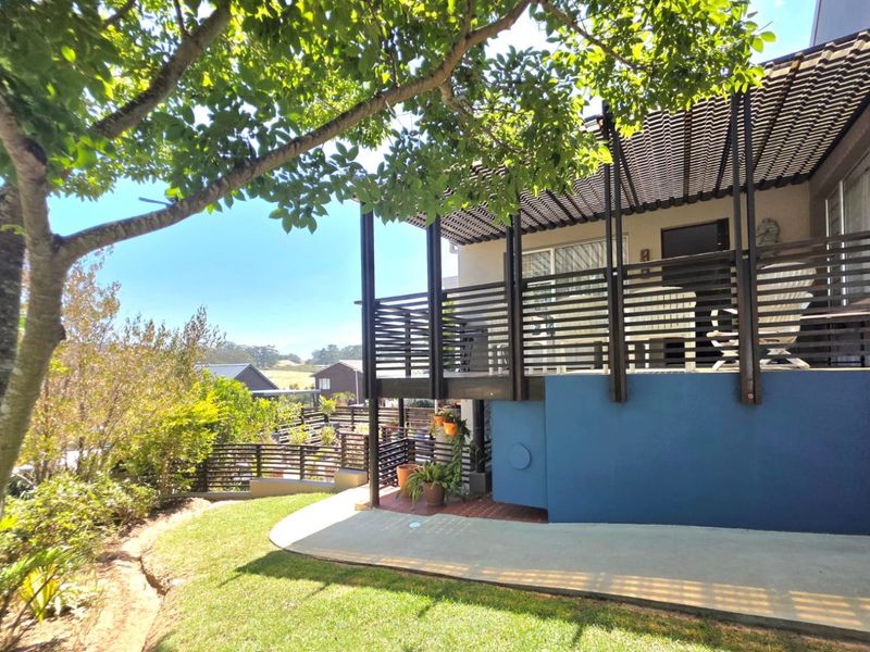 A raised timber deck with a pergola and slatted balustrade, overlooking a landscaped garden and concrete patio area.