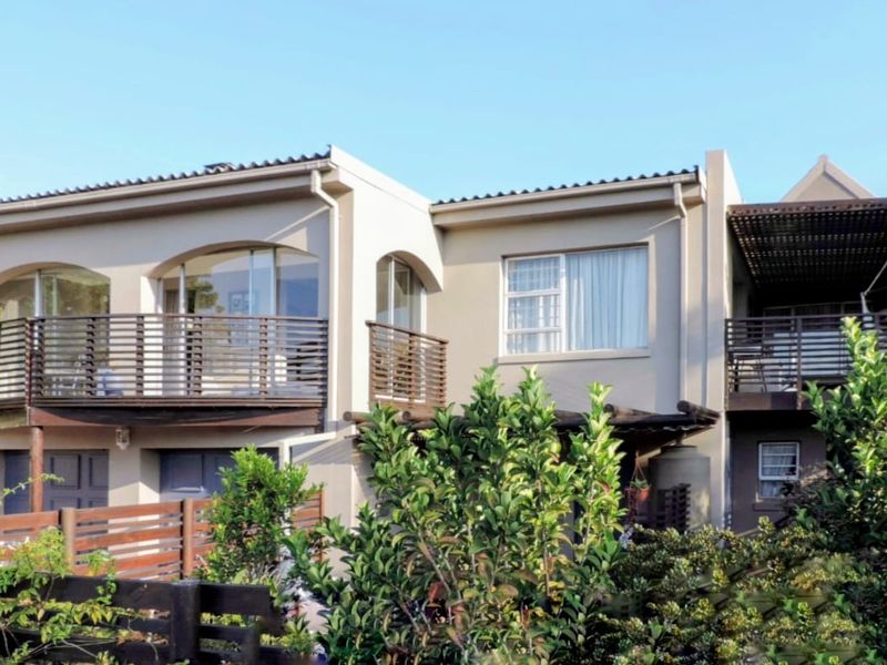 Rear elevation of a multi-story house featuring timber balconies, arched window detailing, and a pergola-covered outdoor area set within a landscaped garden.
