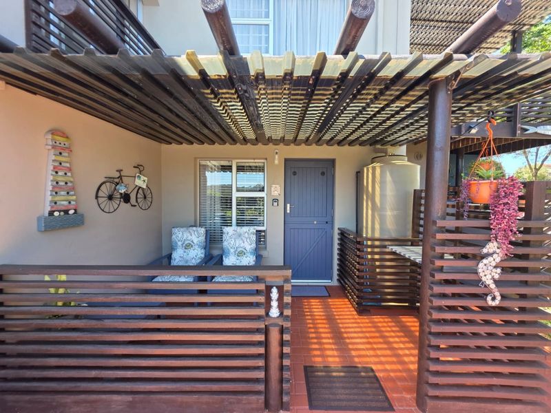 A covered patio area featuring a timber pergola, privacy screening, terracotta tiling, and a built-in water storage tank at the property entrance.