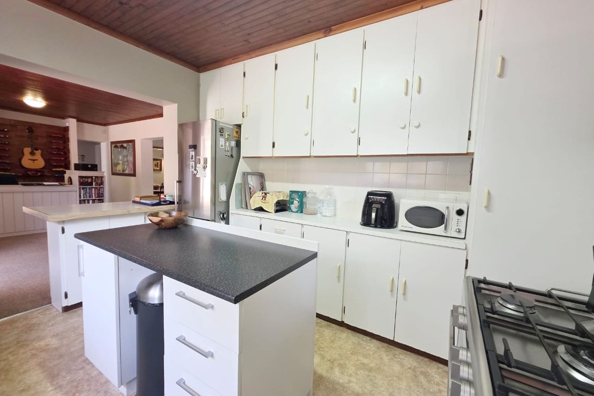 Functional kitchen featuring white cabinetry, a central island with dark countertops, gas cooktop, and a distinctive timber-paneled ceiling.