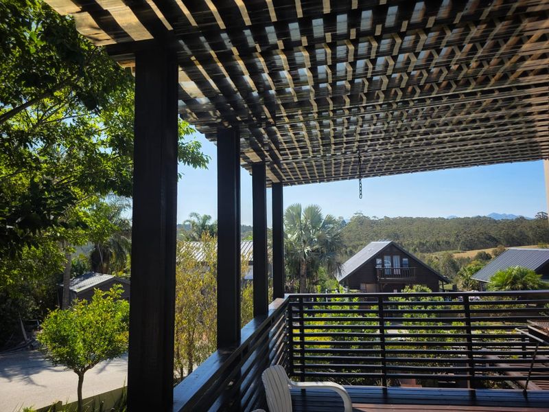 A covered timber balcony featuring a slatted pergola roof and wooden balustrades, offering elevated views of the surrounding landscape.
