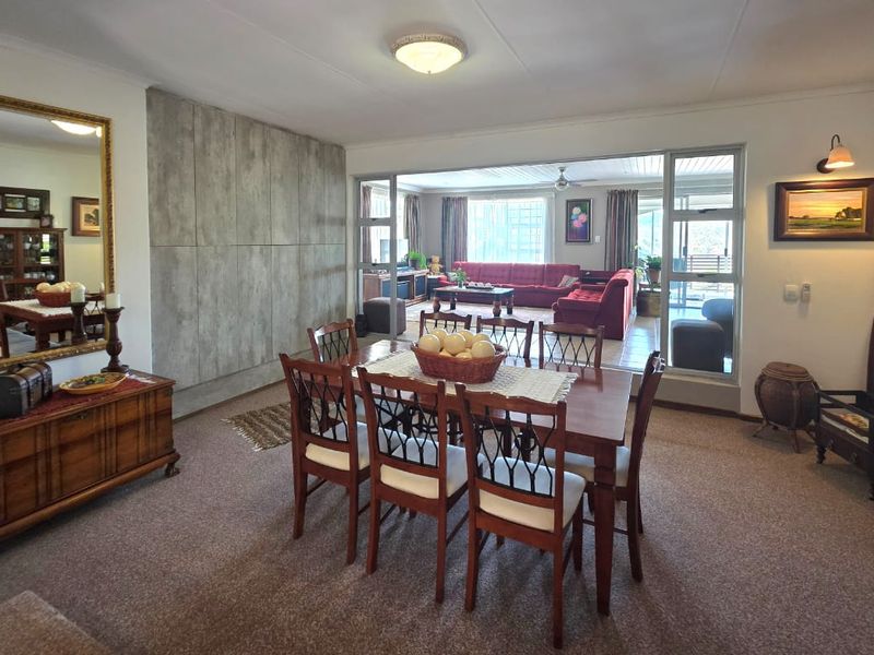 Spacious open-plan dining area featuring a decorative feature wall, carpeted flooring, and large sliding glass doors connecting to an adjacent living space.
