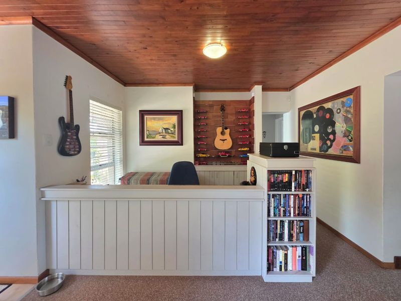 A home office space featuring a timber ceiling, built-in cabinetry, and integrated shelving, providing a functional workspace with natural light.