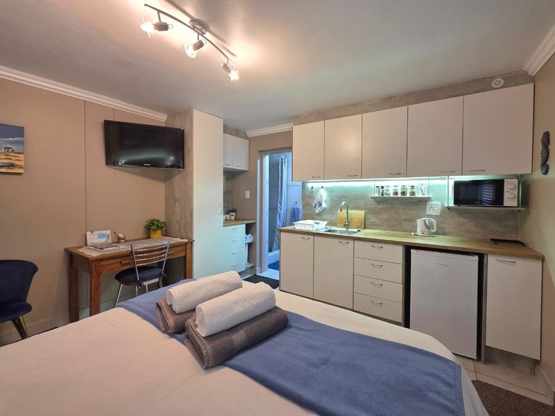 Compact open-plan studio space featuring a kitchenette with built-in cabinetry, laminate countertops, and integrated appliances, leading to an en-suite bathroom.