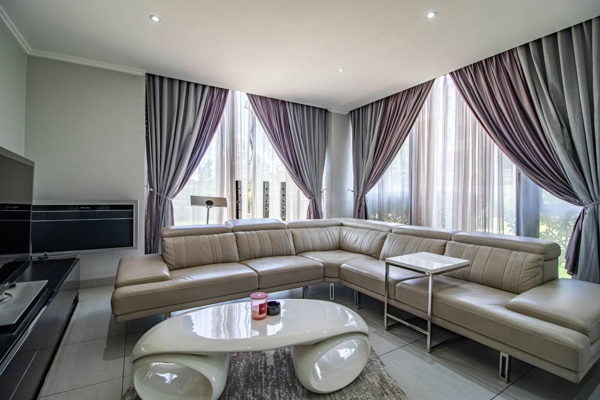 A modern living room featuring large floor-to-ceiling windows with elegant drapery, tiled flooring, and a built-in media console.