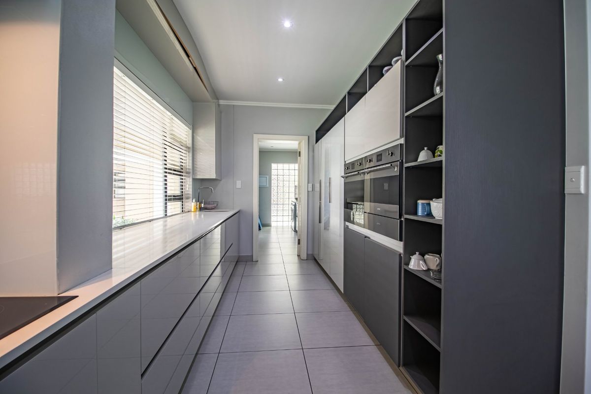 Modern galley-style kitchen featuring high-gloss cabinetry, integrated appliances, quartz countertops, and sleek tiled flooring, offering a clean and contemporary aesthetic.