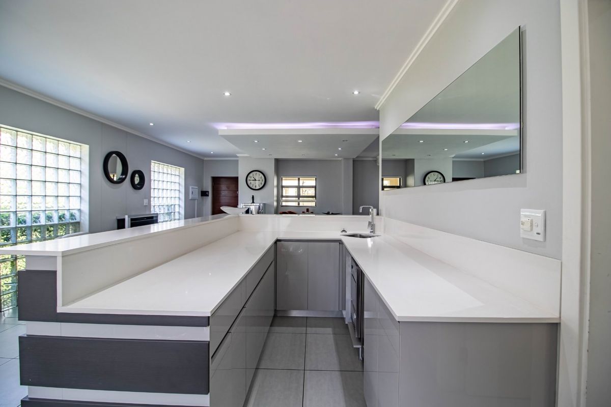 Modern kitchen featuring sleek grey cabinetry, white quartz countertops, an undermount sink, and contemporary recessed and cove lighting.