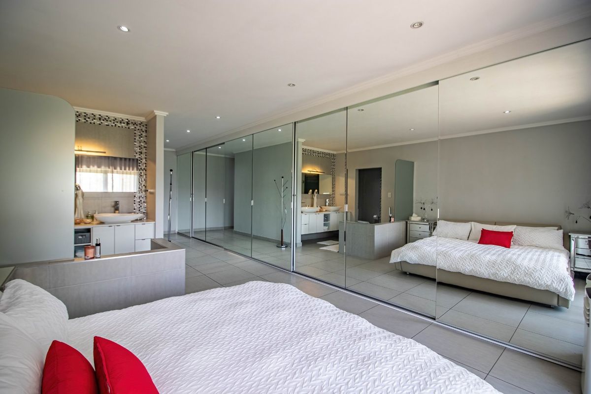 Spacious bedroom featuring large mirrored sliding wardrobes, tiled flooring, recessed lighting, and an integrated vanity area with a modern basin.