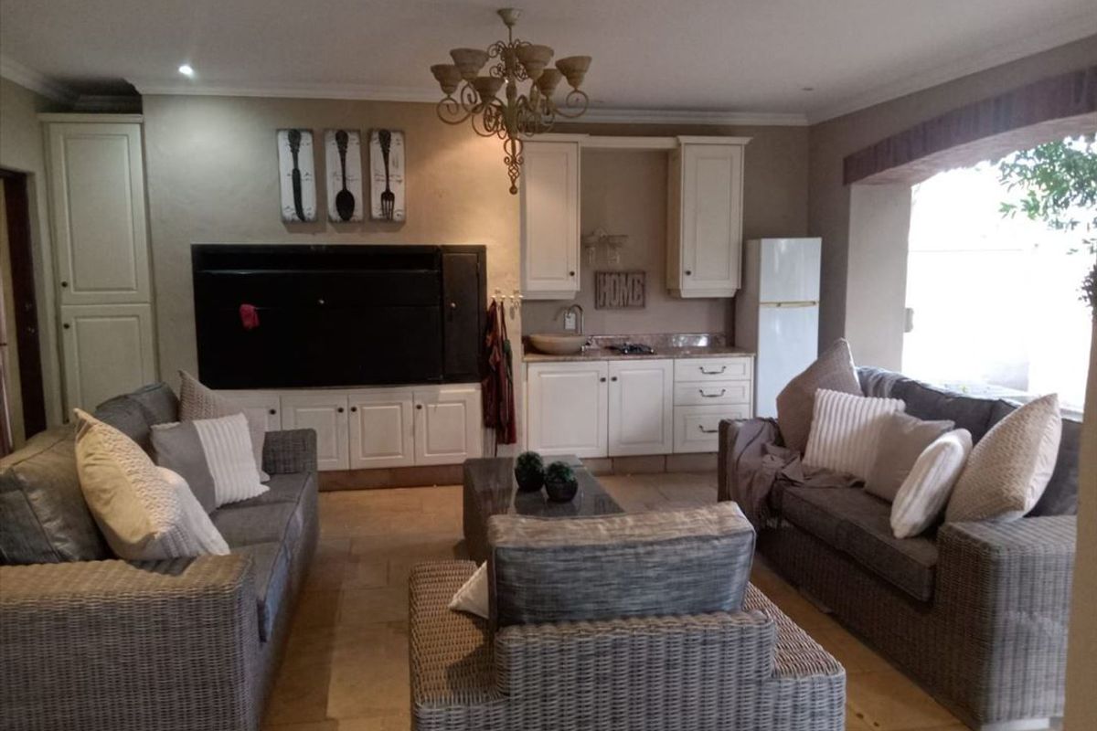 Open plan living area featuring a built-in braai, kitchenette with stone countertops, tiled flooring, and decorative chandelier lighting.