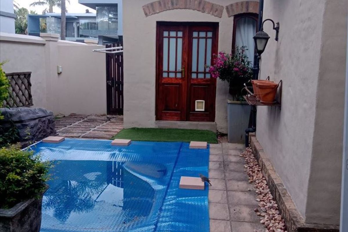 A private outdoor pool area featuring a covered swimming pool, tiled patio space, and direct access to the home through double timber doors.