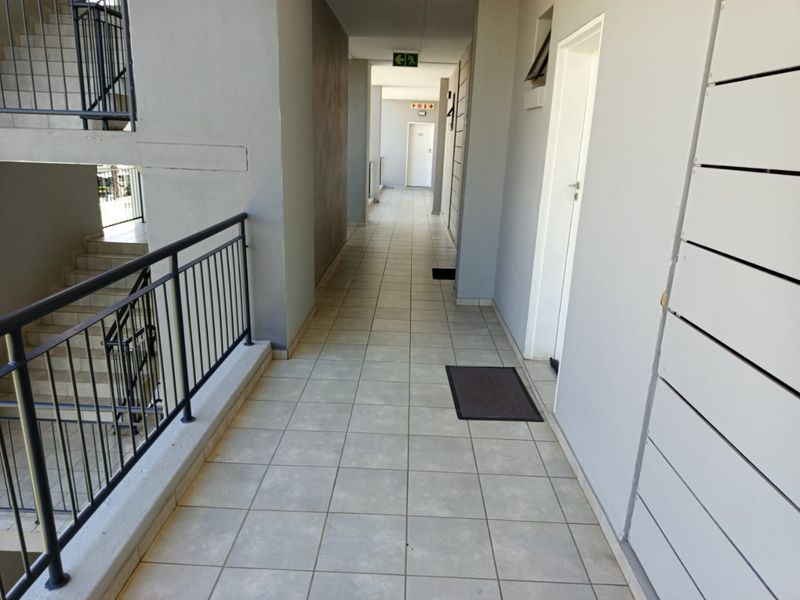 A well-maintained apartment building hallway featuring tiled flooring and a metal balustrade overlooking the staircase.
