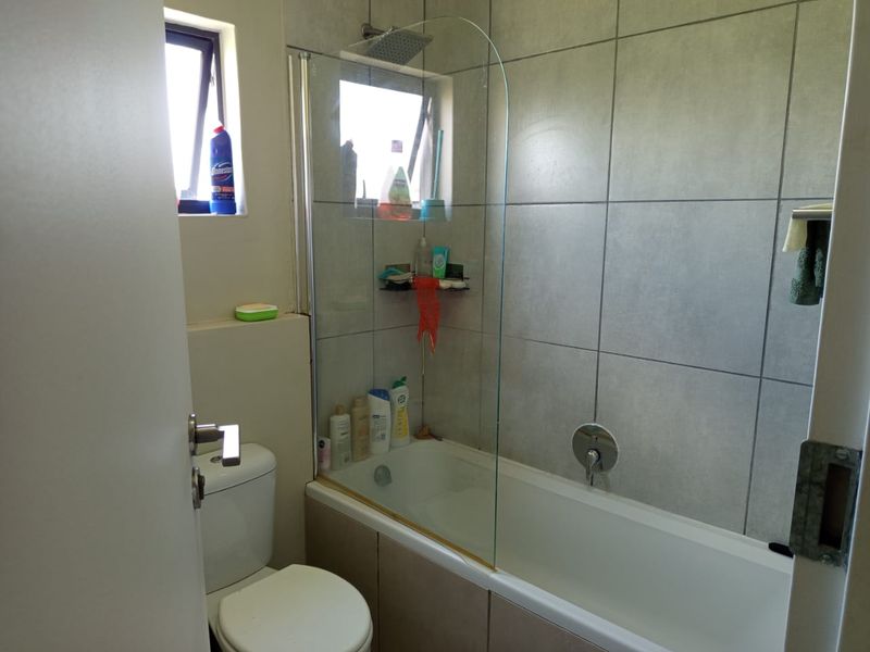 A functional bathroom featuring a bathtub with an integrated shower, glass screen, and neutral wall tiling.