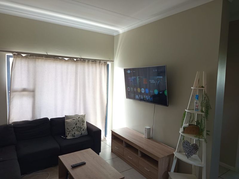 A living room featuring tiled flooring, coving, and a wall-mounted television, providing a functional and comfortable space.