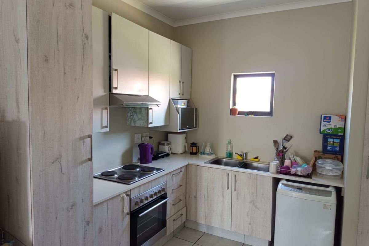 A functional kitchen featuring light wood-look cabinetry, integrated appliances including an oven and hob, double sink, and tiled flooring.