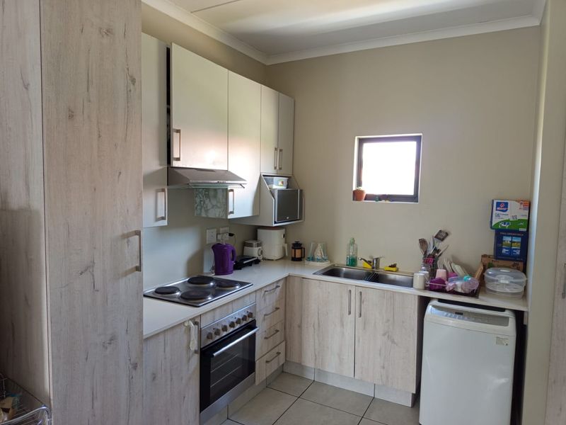 A functional kitchen featuring light wood-look cabinetry, integrated appliances including an oven and hob, double sink, and tiled flooring.