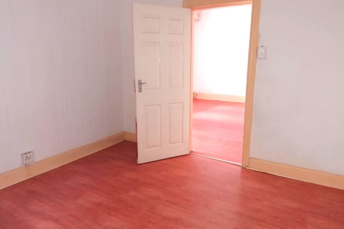 An empty bedroom featuring laminate flooring and a standard internal door, leading into an adjacent room.