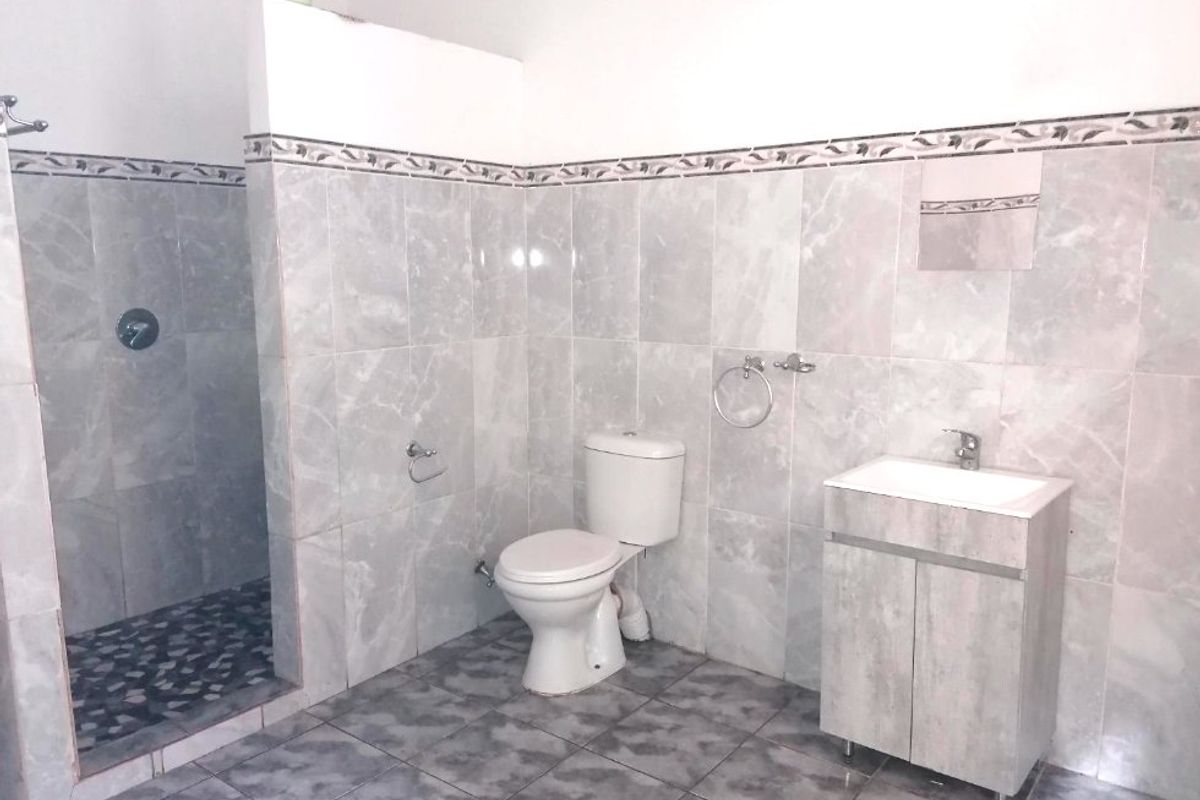A functional bathroom featuring a walk-in shower with pebble flooring, a vanity unit with basin, and a standard toilet, finished with grey wall tiles.
