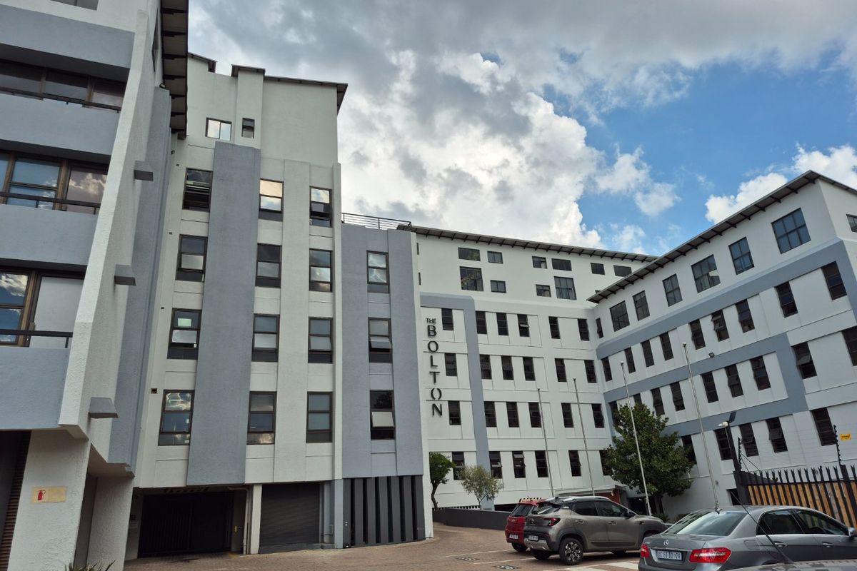 Exterior view of The Bolton apartment complex, showcasing the multi-story building facade, paved parking area, and modern architectural design.