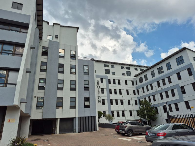 Exterior view of The Bolton apartment complex, showcasing the multi-story building facade, paved parking area, and modern architectural design.