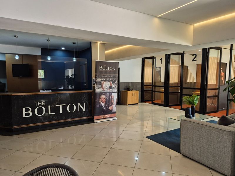Modern apartment building reception area featuring a branded front desk, tiled flooring, and glass-partitioned office or meeting spaces.
