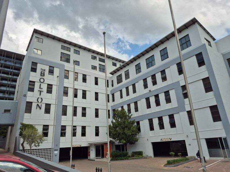 Exterior view of The Bolton apartment building, showcasing the multi-story facade, entrance area, and ground-level parking access.