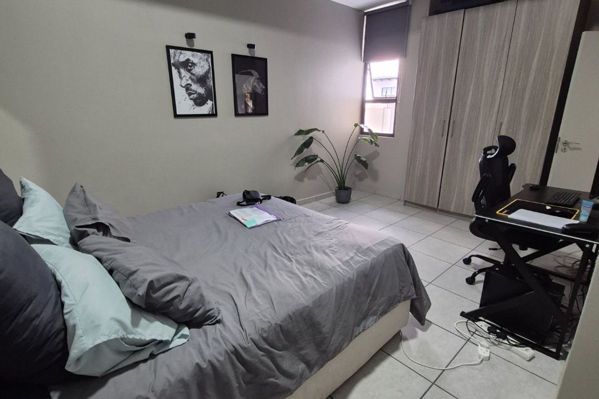 A well-lit bedroom featuring neutral tiled flooring, built-in wooden cabinetry, and a window with a roller blind.