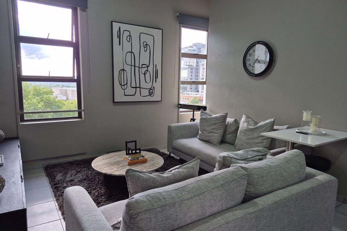 A bright and modern living room featuring large windows with urban views, neutral wall tones, and tiled flooring.