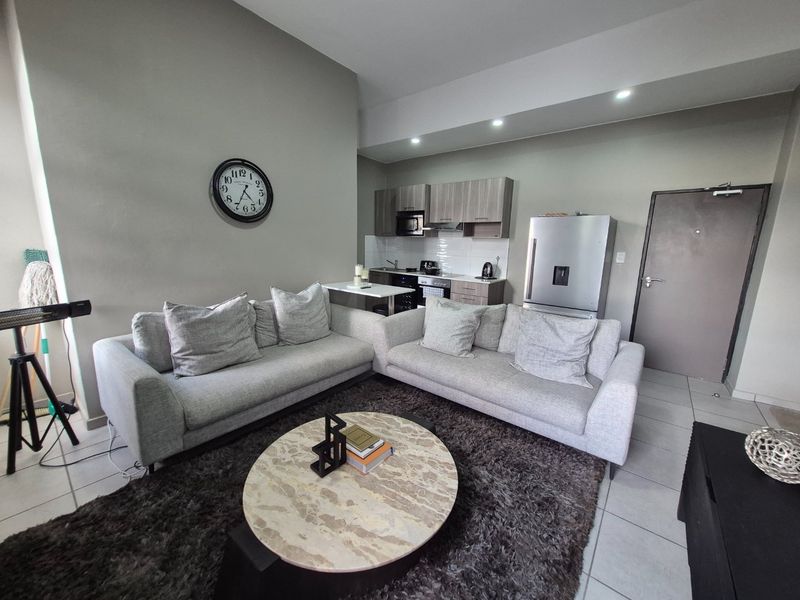 Open-plan living area featuring a modern kitchen with built-in cabinetry, integrated appliances, and tiled flooring throughout.