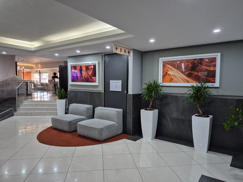 A modern apartment building lobby featuring tiled flooring, recessed ceiling lighting, and stone wall cladding, providing a clean and professional entrance area.