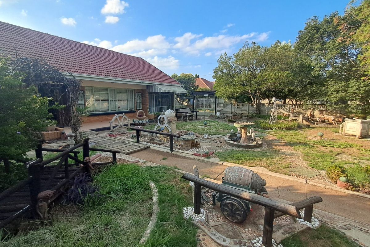 Spacious rear garden area featuring paved pathways, established trees, and a brick-built house with a tiled roof.