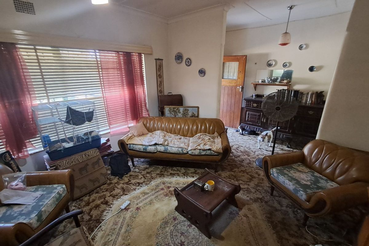 A living room featuring dated carpet flooring, timber door, and venetian blinds, offering a blank canvas for modernization and renovation.