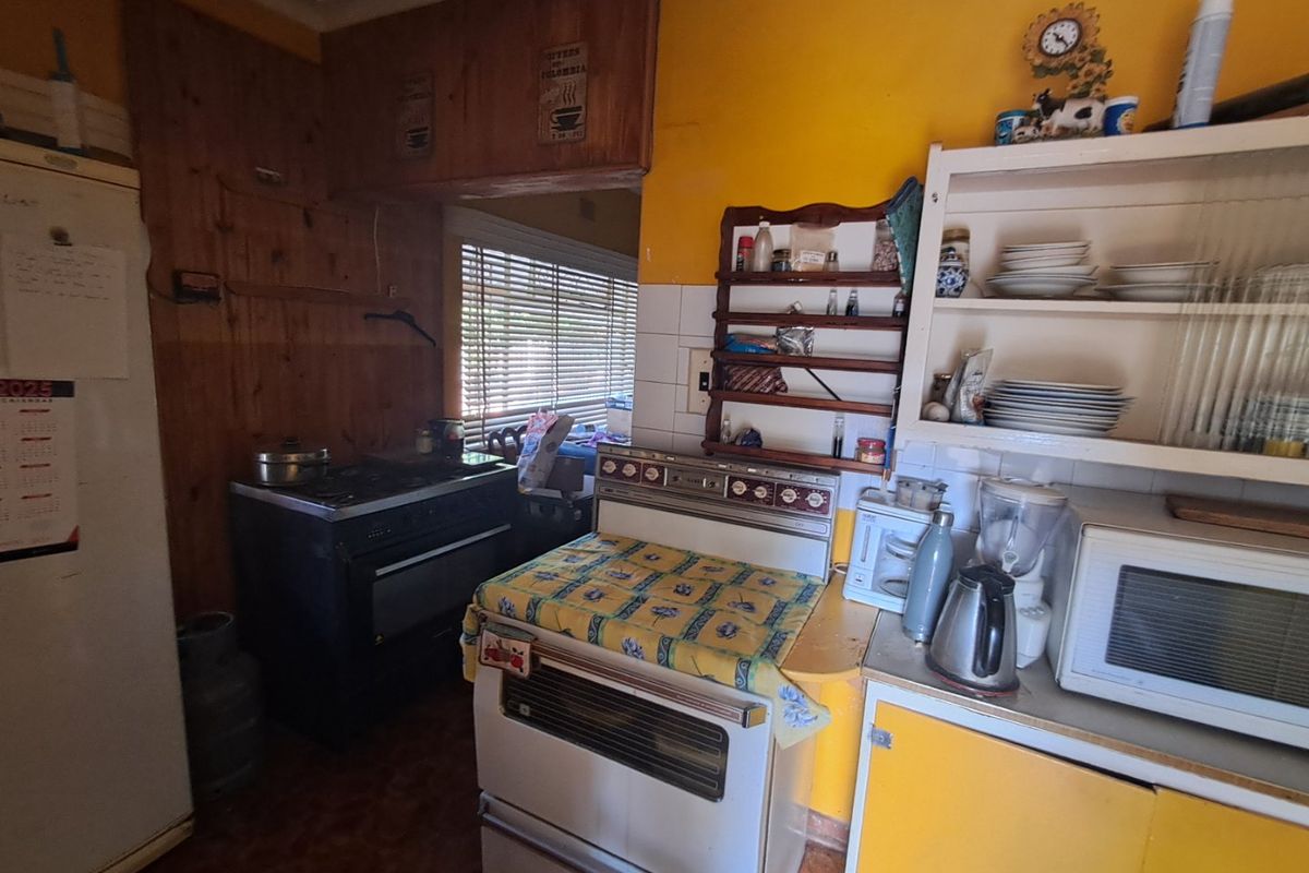 A dated kitchen featuring timber wall paneling, yellow walls, and traditional built-in appliances, offering significant potential for a modern renovation.