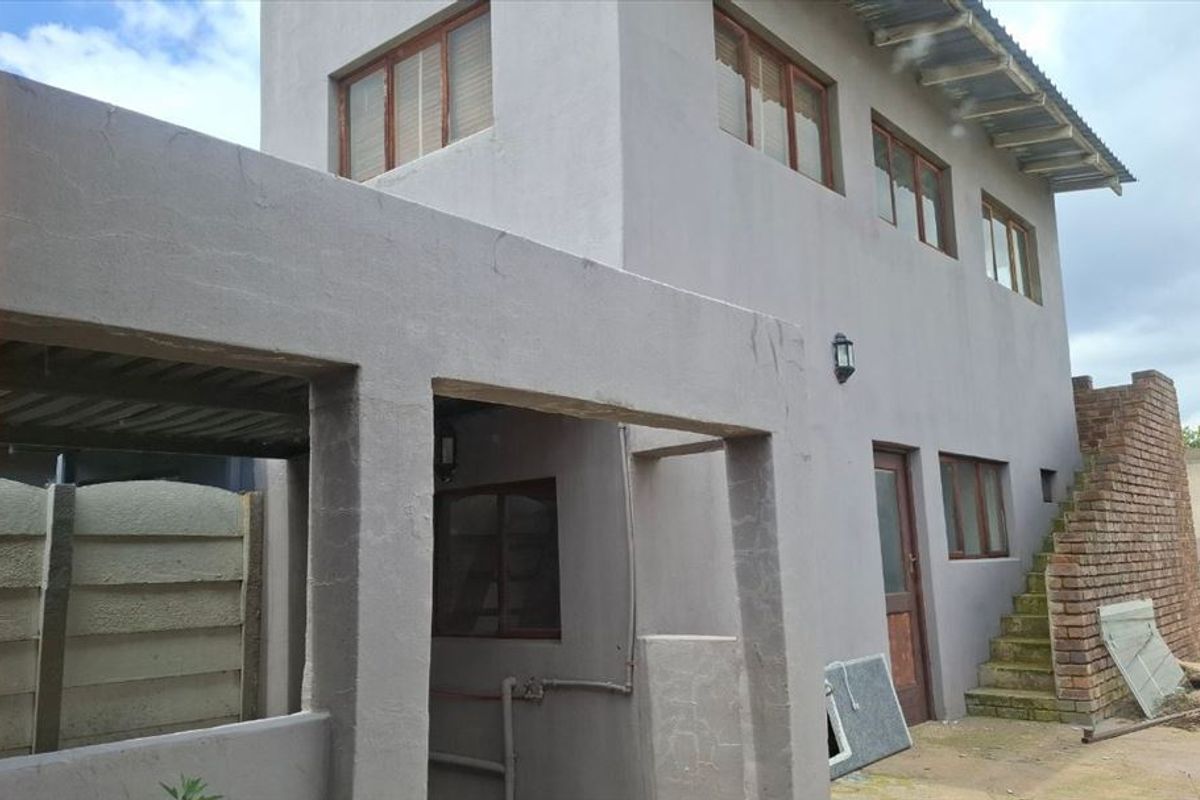Rear view of a two-story house featuring a covered patio area, external staircase, and exposed brickwork, showing signs of wear and maintenance requirements.