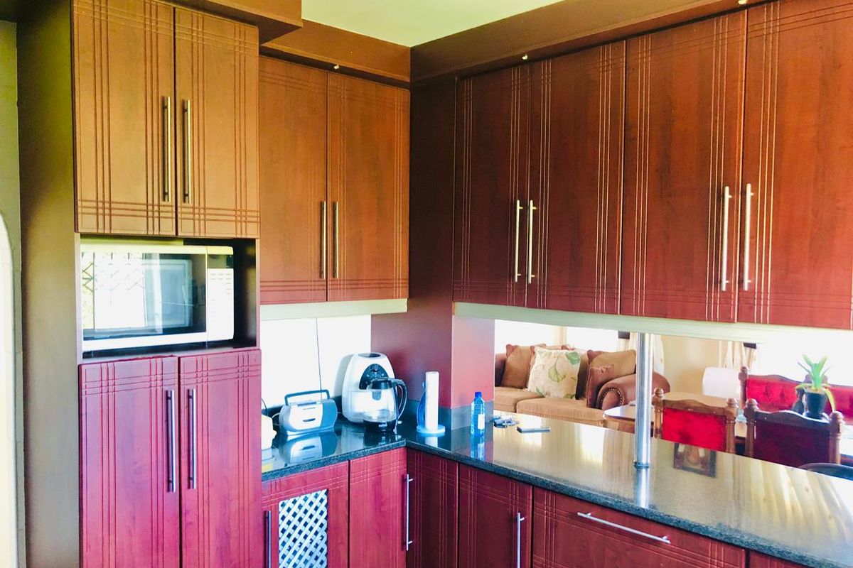 A kitchen featuring dark wood cabinetry, granite countertops, and a built-in microwave, with a breakfast bar overlooking the adjacent living area.
