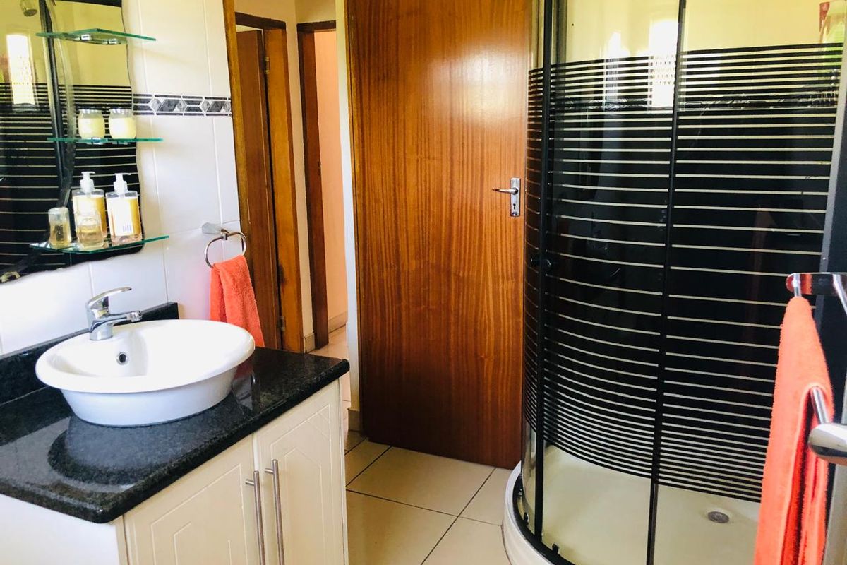 A functional bathroom featuring a vanity with a vessel sink, a corner shower enclosure with a striped screen, and tiled flooring.